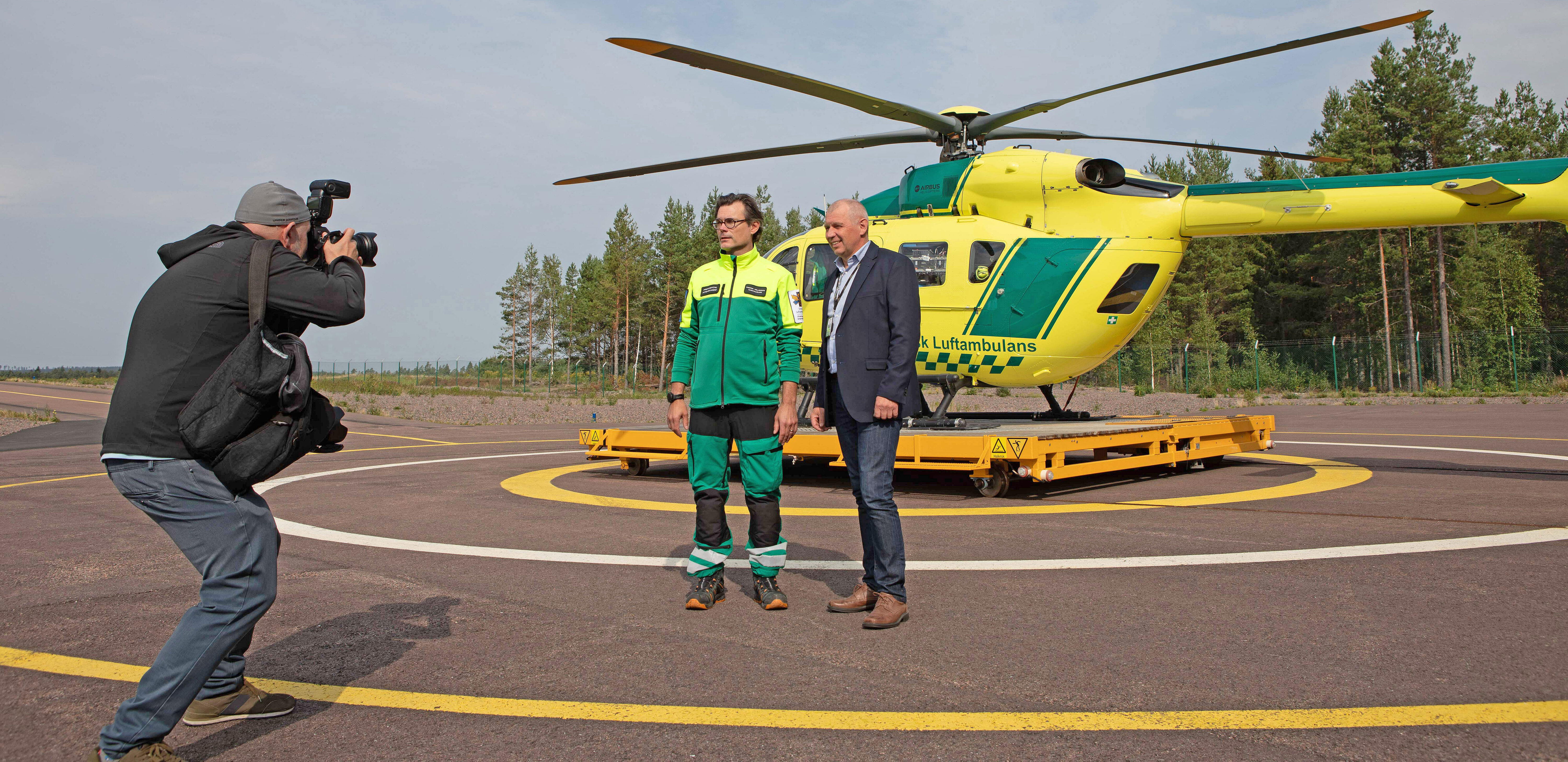 En fotograf tar en bild av Fredrik Helliksson och Lars-Olof Björkqvist vid en gul helikopter.