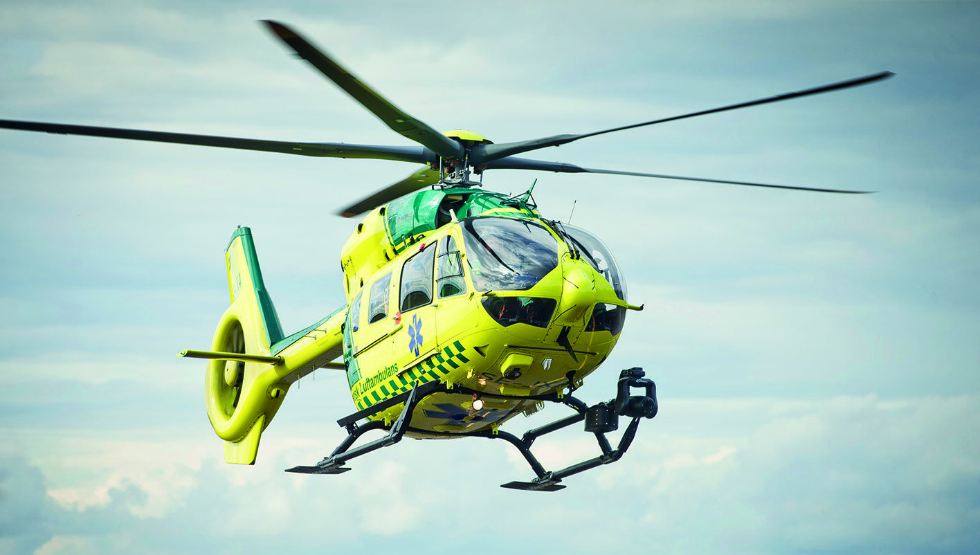 Gul ambulanshelikopter mot molnig himmel.
